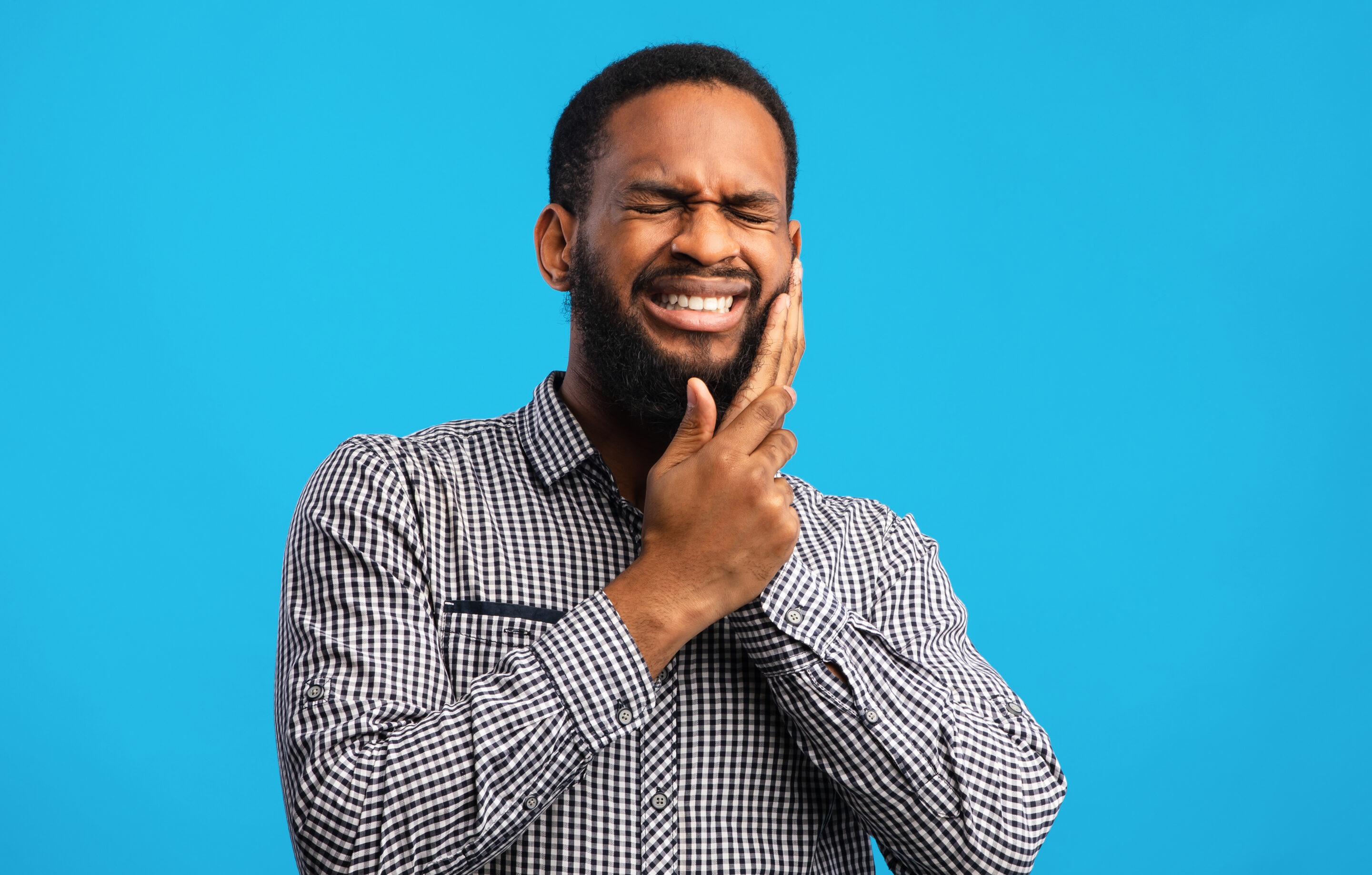 Smiling man in striped shirt touching face against blue background for dental care website.